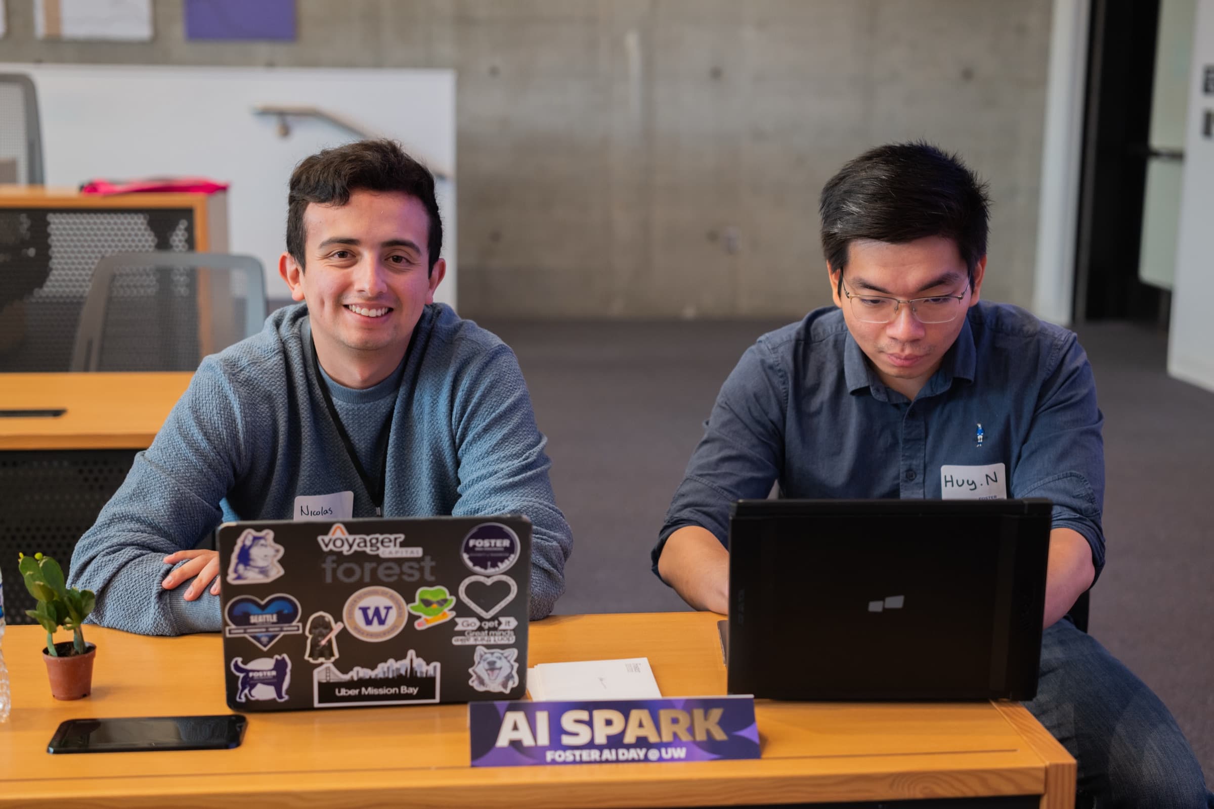 Nicolas at a laptop alongside another person in the AI Spark hackathon room.