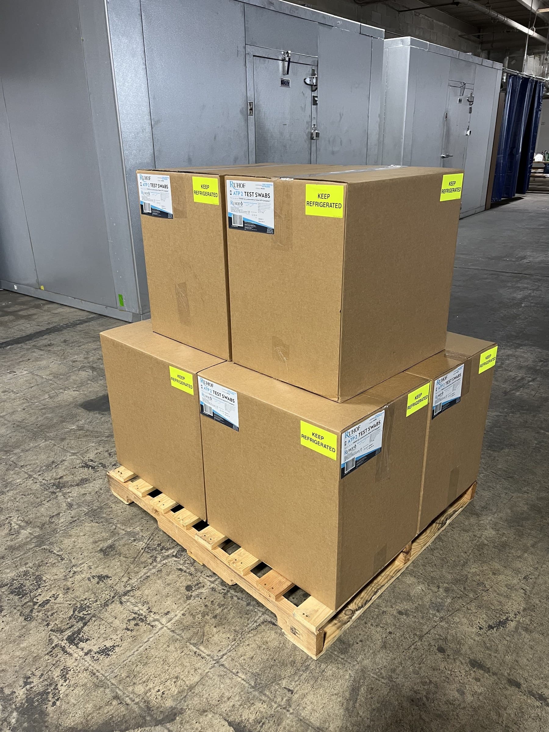 Boxes of ATP test swabs stacked on a pallet near refrigeration units.