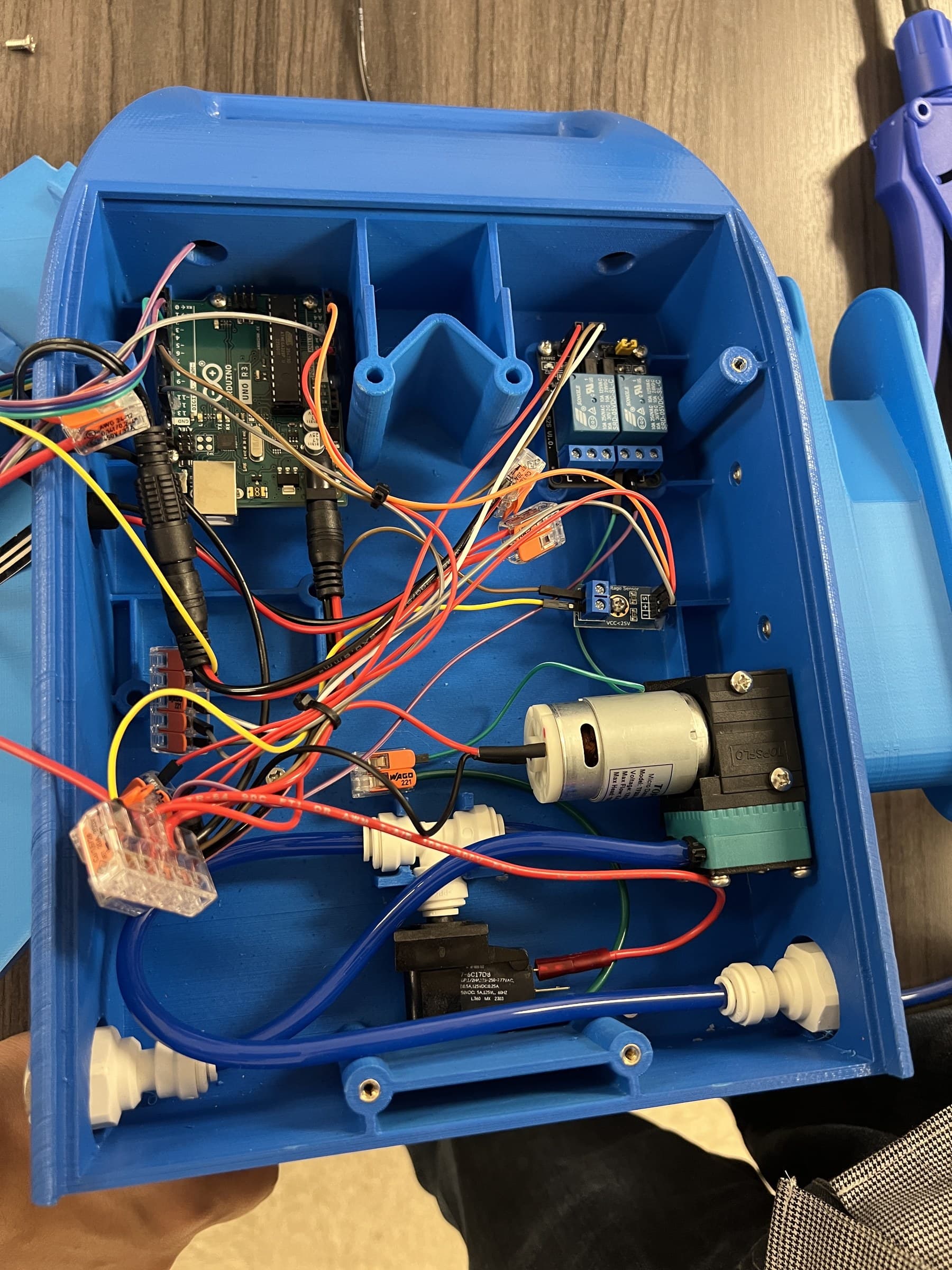 Arduino board, relays, tubing, and a pump mounted inside a blue enclosure.